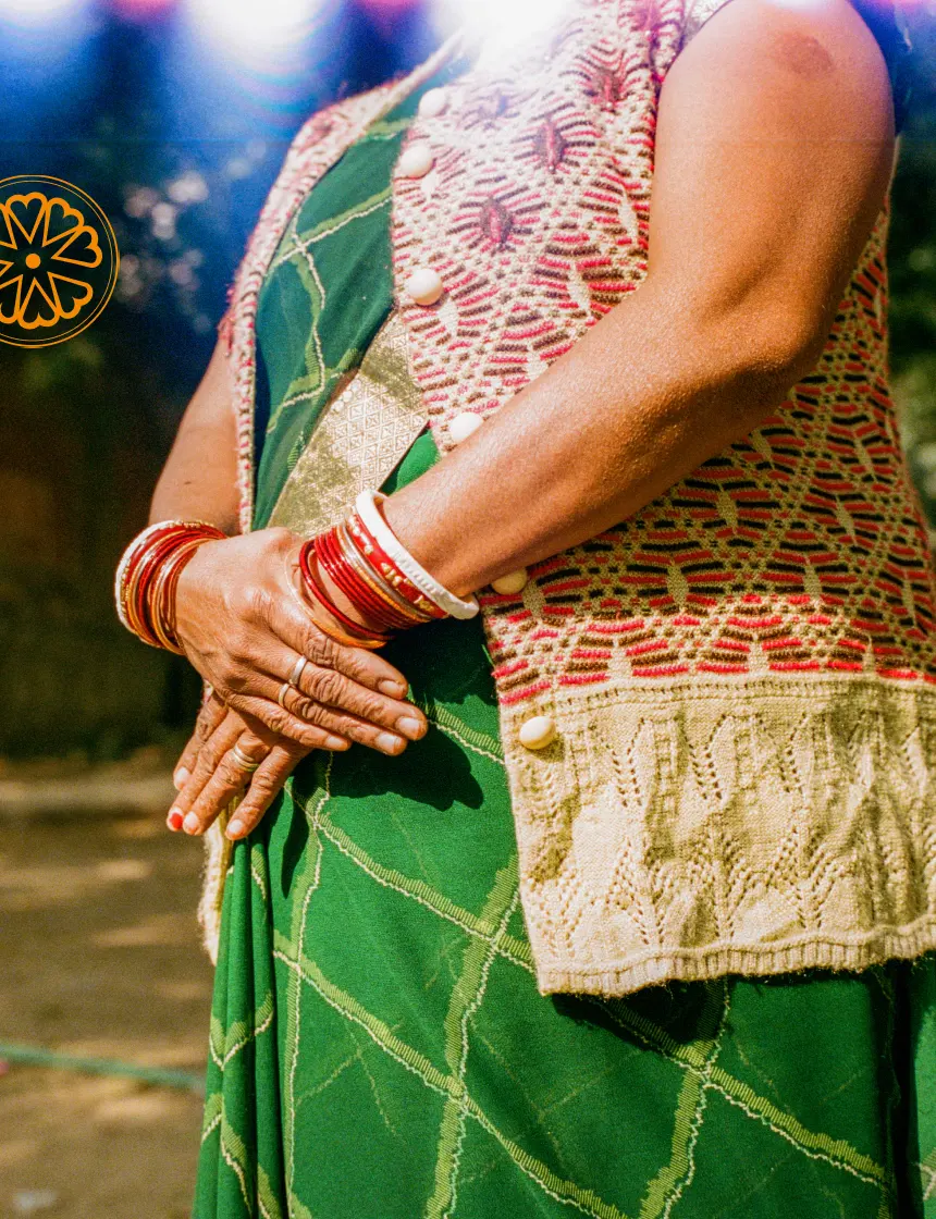 Woman wearing traditional green and red patterned clothing and red bangles.